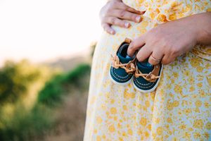 Hands holding a yellow floral patterned dress against a sunlit garden background.