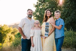 A family group poses together outdoors during golden hour in casual clothing against a natural backdrop.