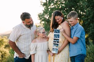 A group stands outdoors looking at ultrasound photos together in a heartfelt pregnancy announcement moment.