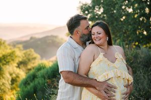 A couple kissing outdoors against a backdrop of lush vegetation and warm evening sunlight.