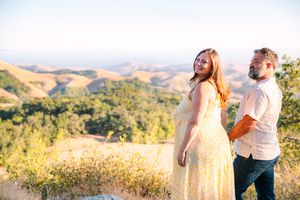 Young couple enjoys a romantic moment in golden sunlight on a hilltop overlooking rolling countryside.