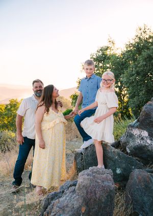 Family sitting together on large rocks during golden hour sunset photo session in nature setting.