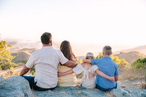 Family enjoying sunset view sitting on rocks overlooking scenic desert mountains and valley below.