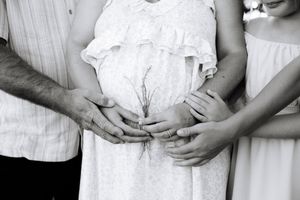 A series of five black and white photos showing hands gently cradling pregnant bellies in different poses.