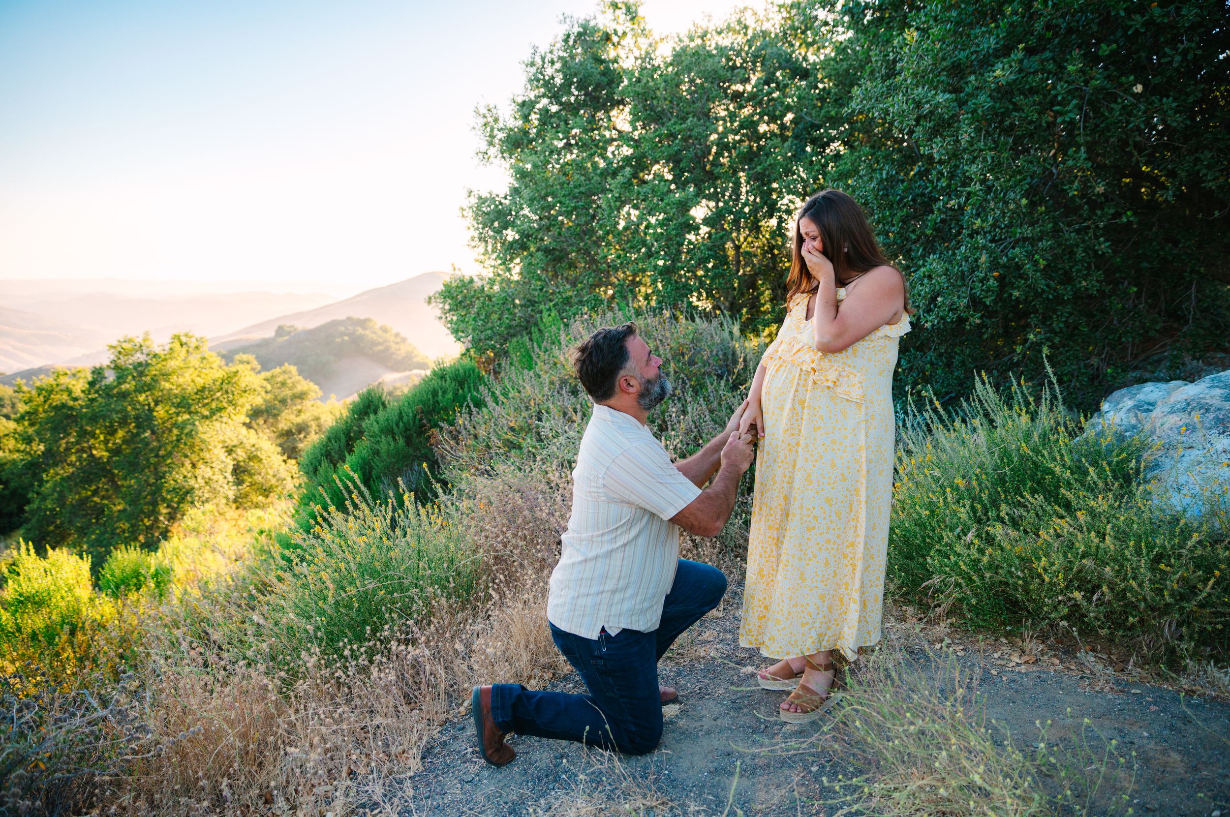 A couple shares a romantic moment on a hilltop trail during golden hour as sunlight illuminates the natural landscape.