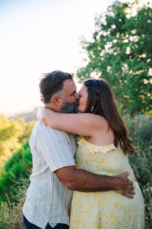 A couple sharing a romantic embrace in a sunlit garden setting with green foliage in the background.