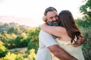 Joyful couple embraces during golden hour photoshoot in a scenic outdoor setting with rolling hills in background.