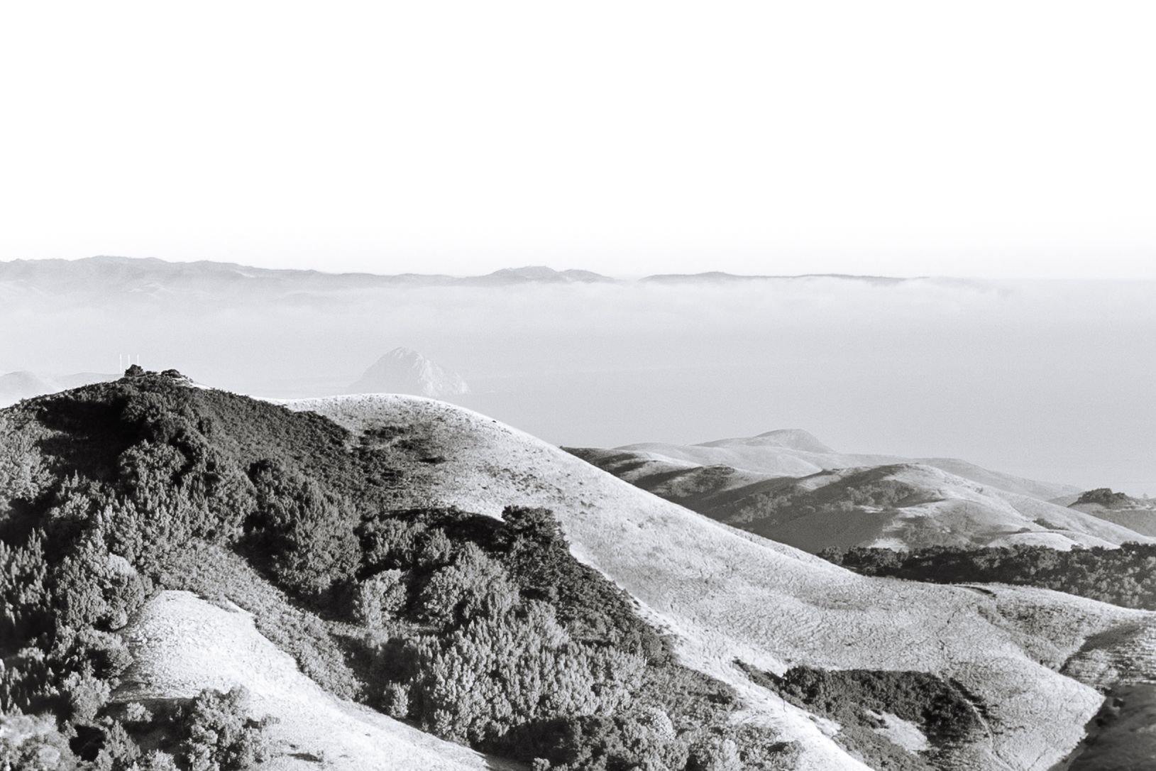Aerial view of rugged mountain ridges with snow patches and winding trails across the rocky terrain.