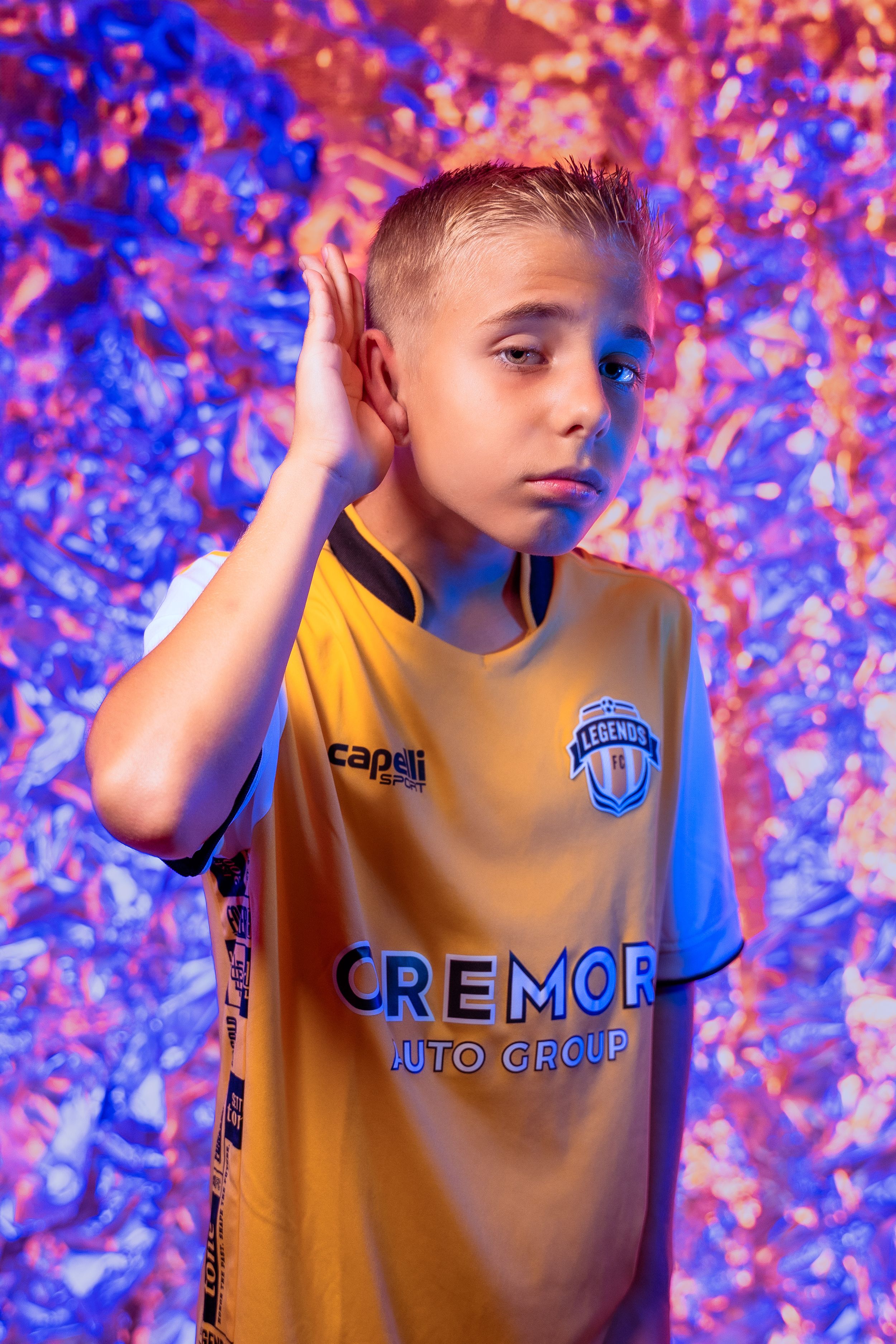 Soccer athlete wearing yellow Legends FC jersey poses against vibrant pink and blue confetti background.