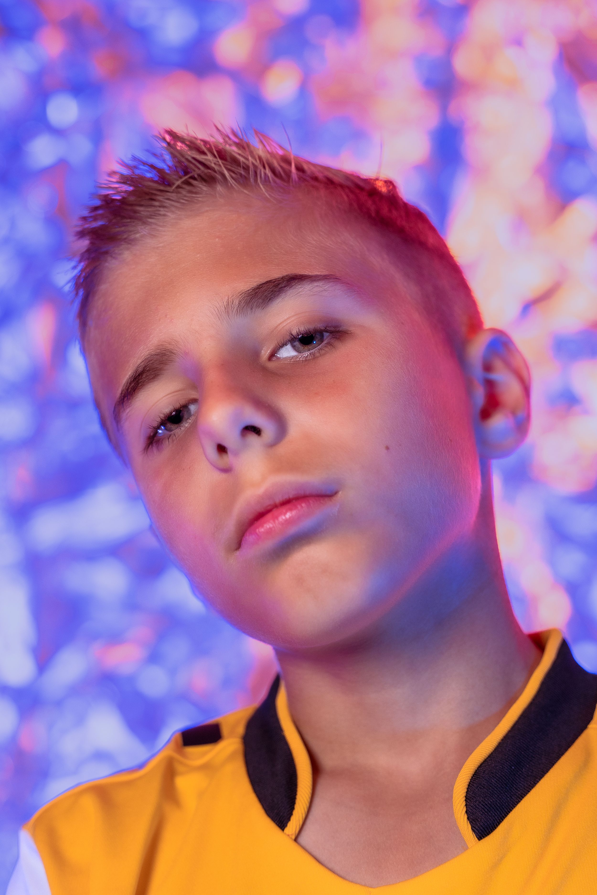 Young soccer player in dramatic lighting with pink and blue backdrop.