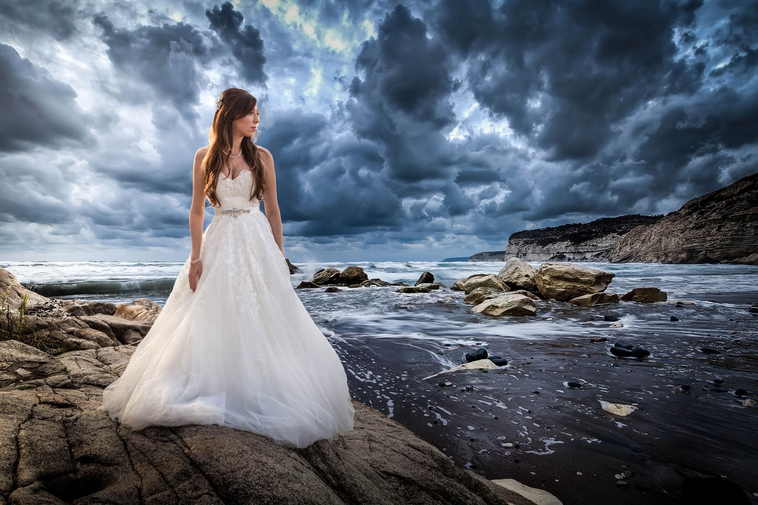 Dramatic coastal wedding photography with stormy clouds and rocky shoreline.