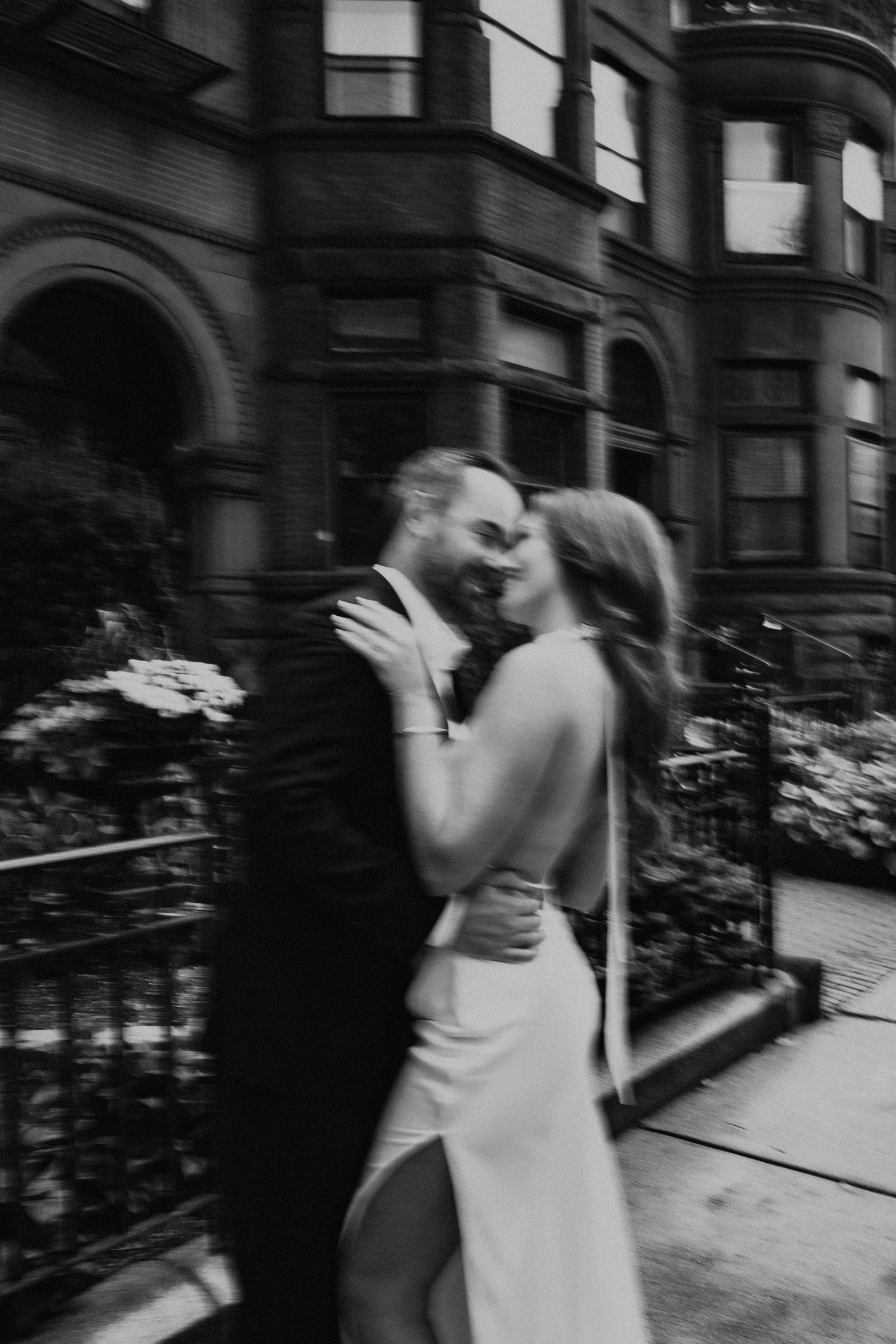 A romantic black and white wedding photograph showing an intimate moment outside a brownstone building.