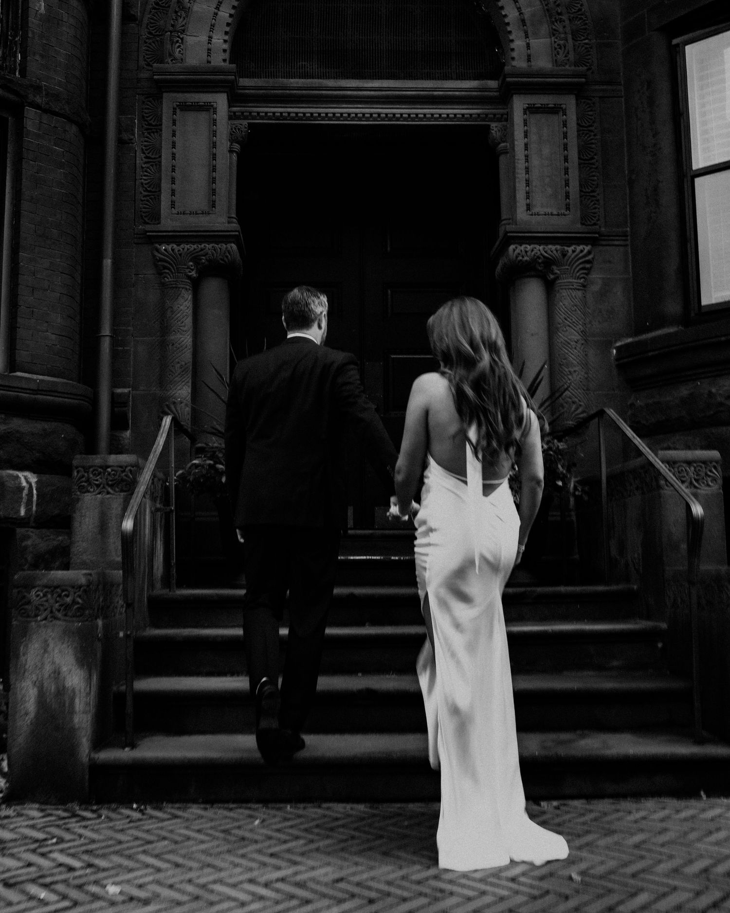 Romantic scene on brick stairs of historic brownstone building with white gown trailing down steps.