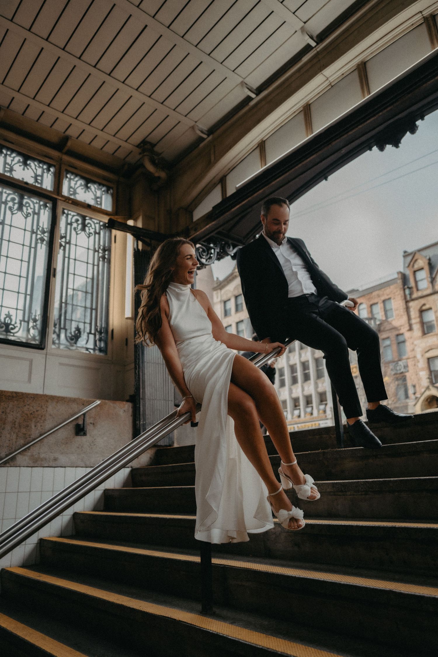 Romantic wedding couple performs a playful dance pose on historic wooden stairs in vintage building interior.