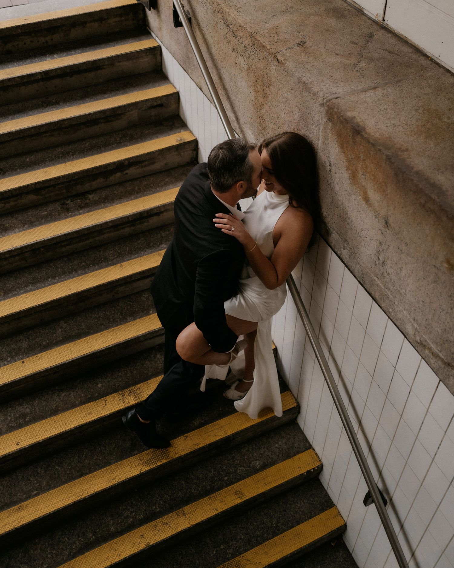 A couple embraces on wooden stairs captured in a moody, dark style photography composition.