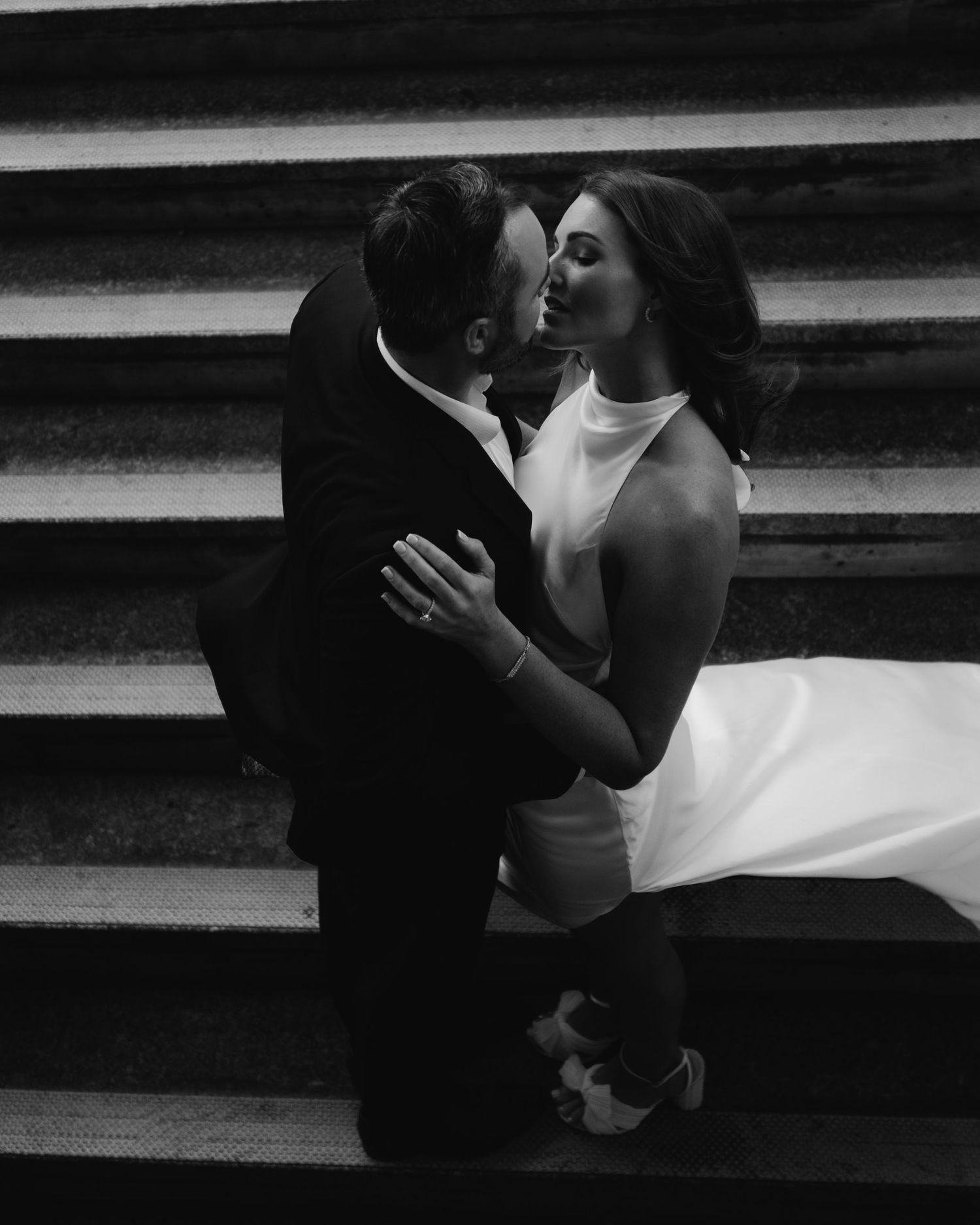 Romantic black and white image of couple embracing on grand stone steps.