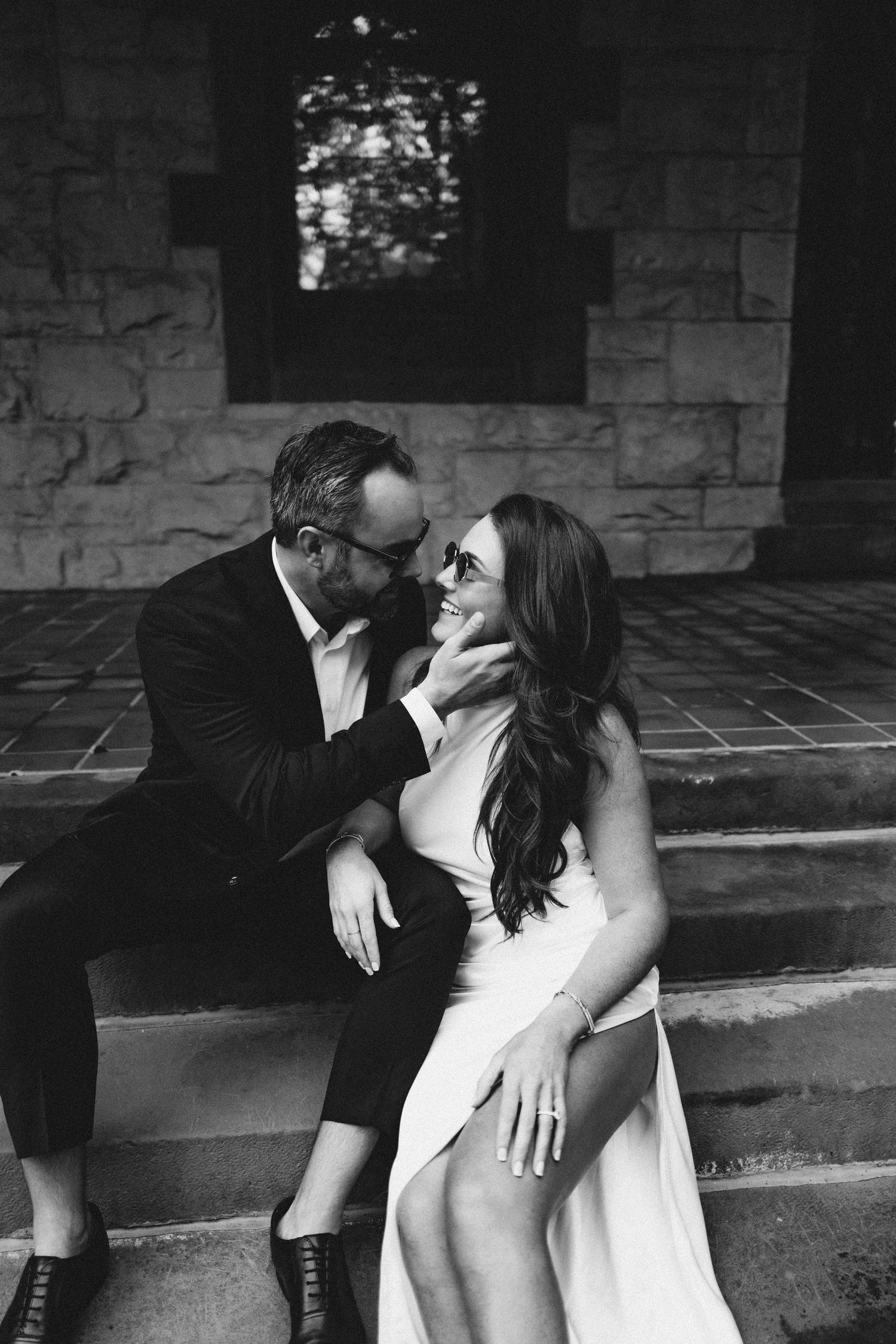 Black and white photo series showing intimate romantic moments between a couple seated against a stone wall.