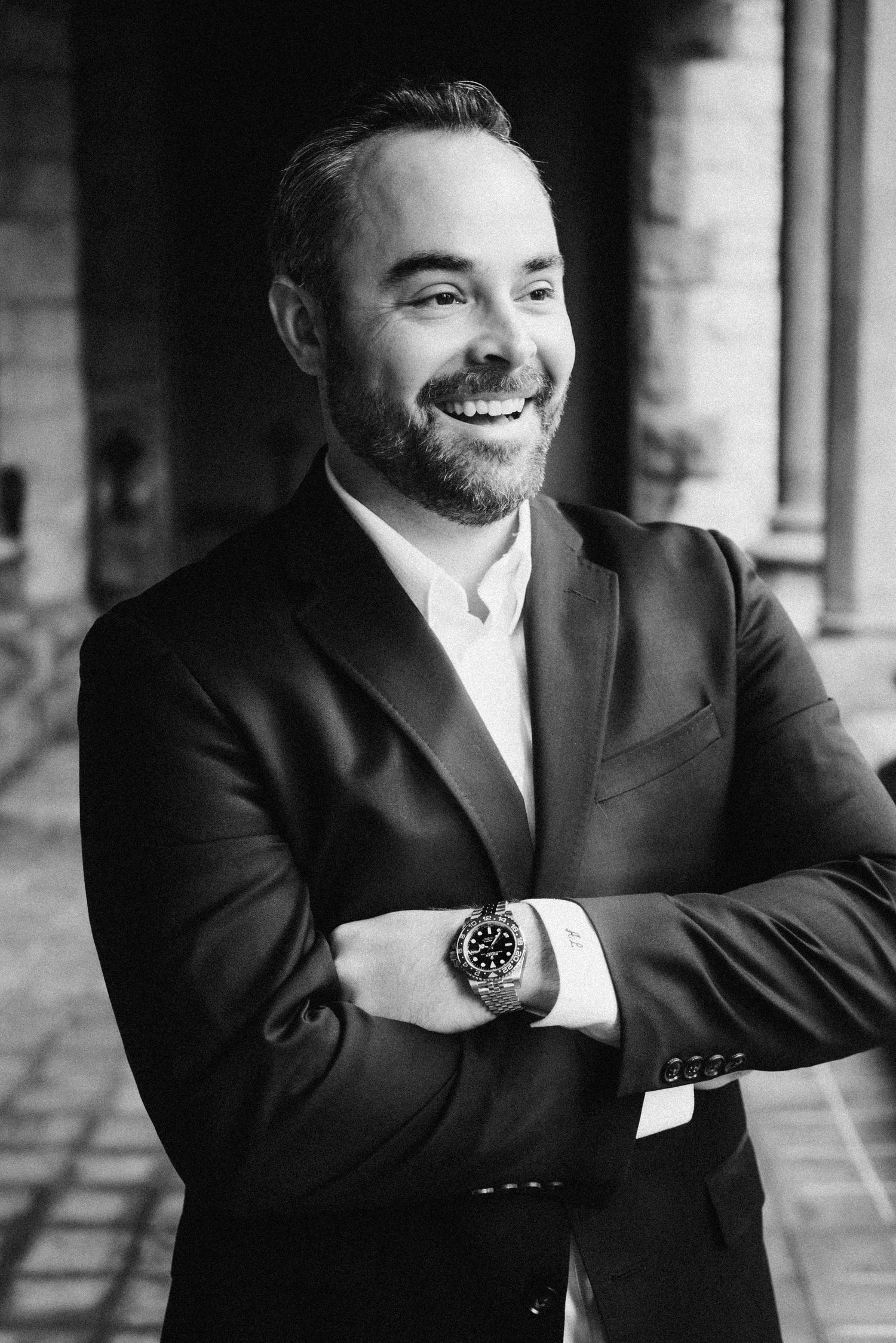 Four black and white portraits of a smiling person in a suit posing in different poses by a window.