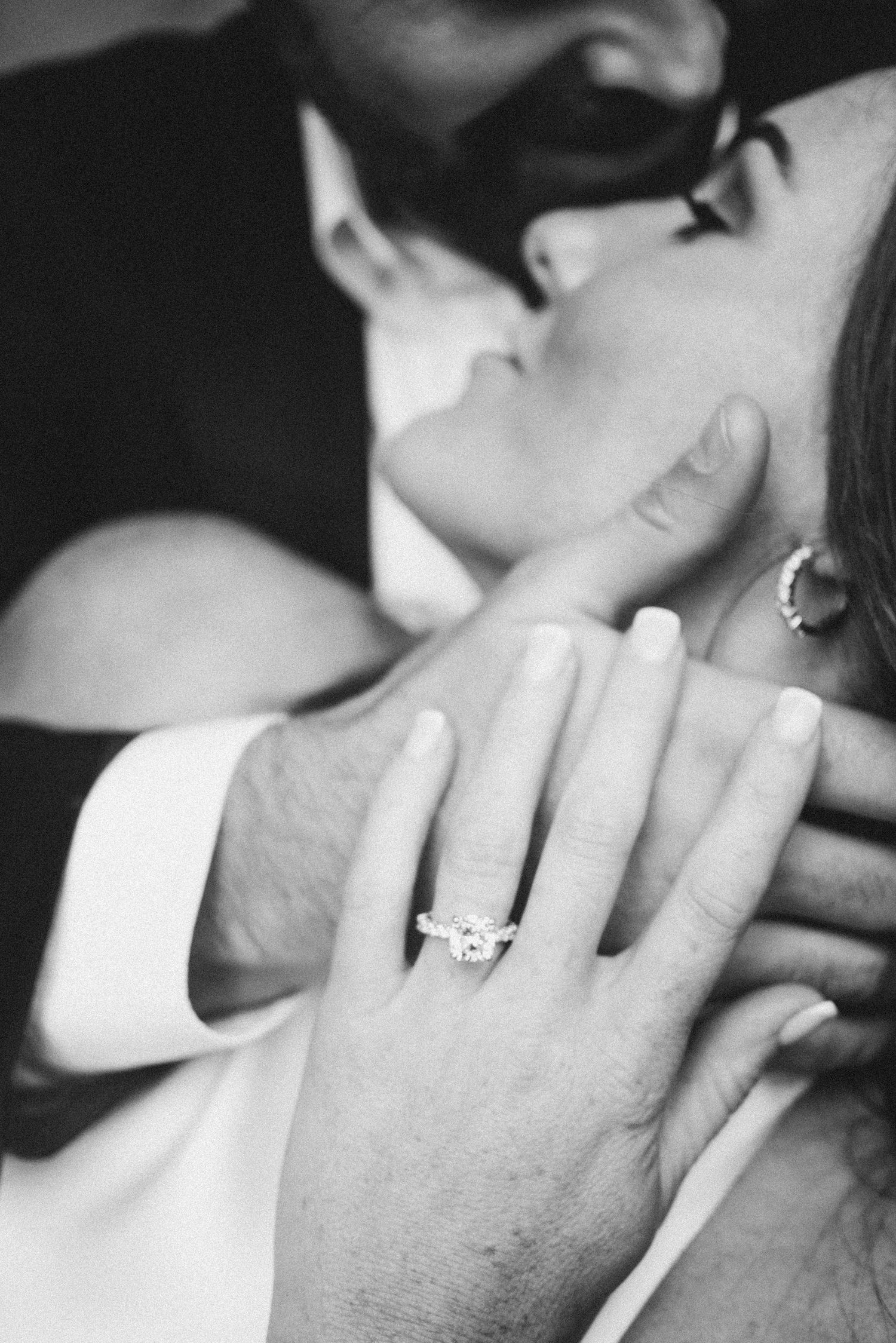 Four black and white film photos showing a romantic kiss with an engagement ring on display.