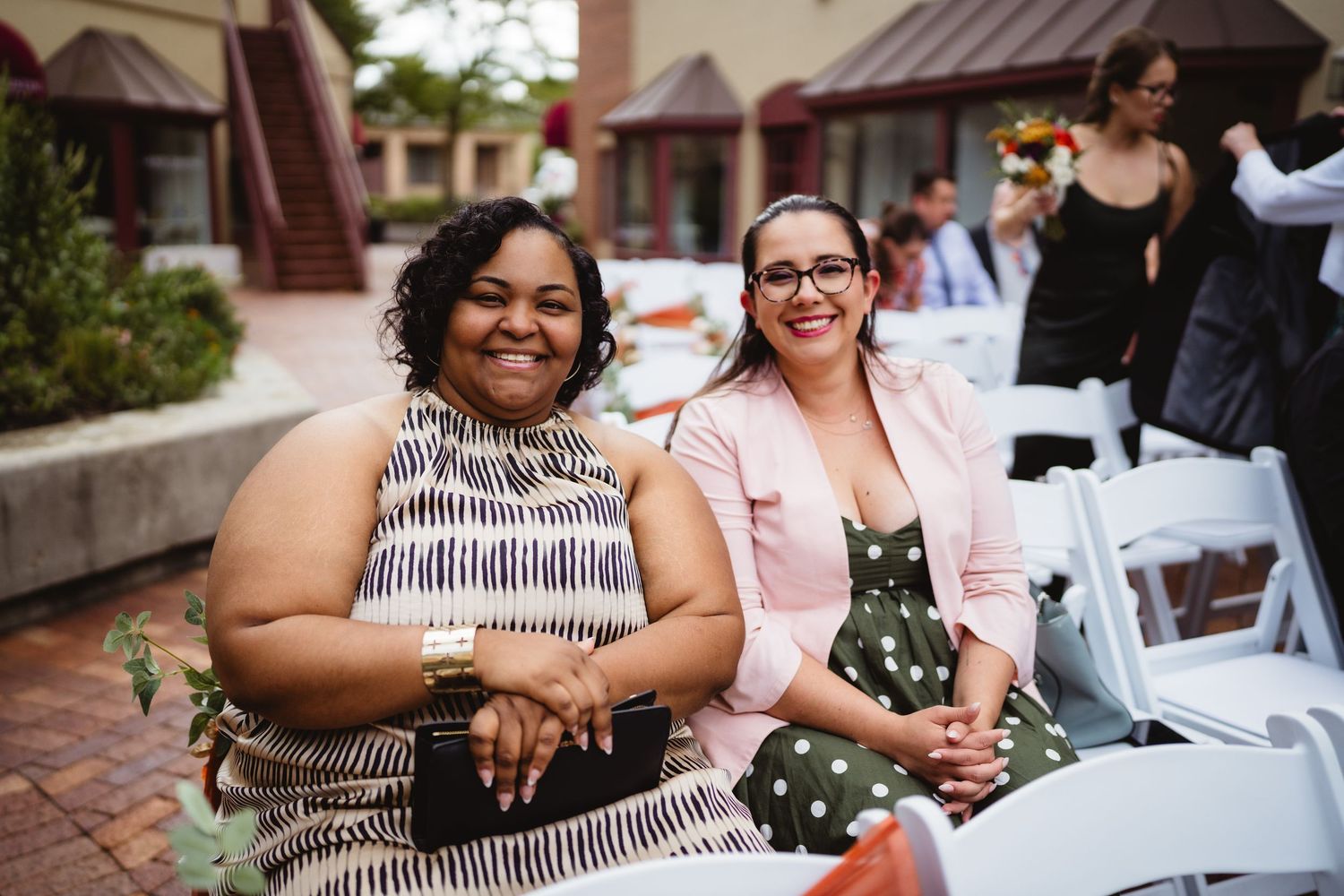 Wedding guests enjoy outdoor reception on a beautiful sunny day at a venue with brick pathways and rustic decor.