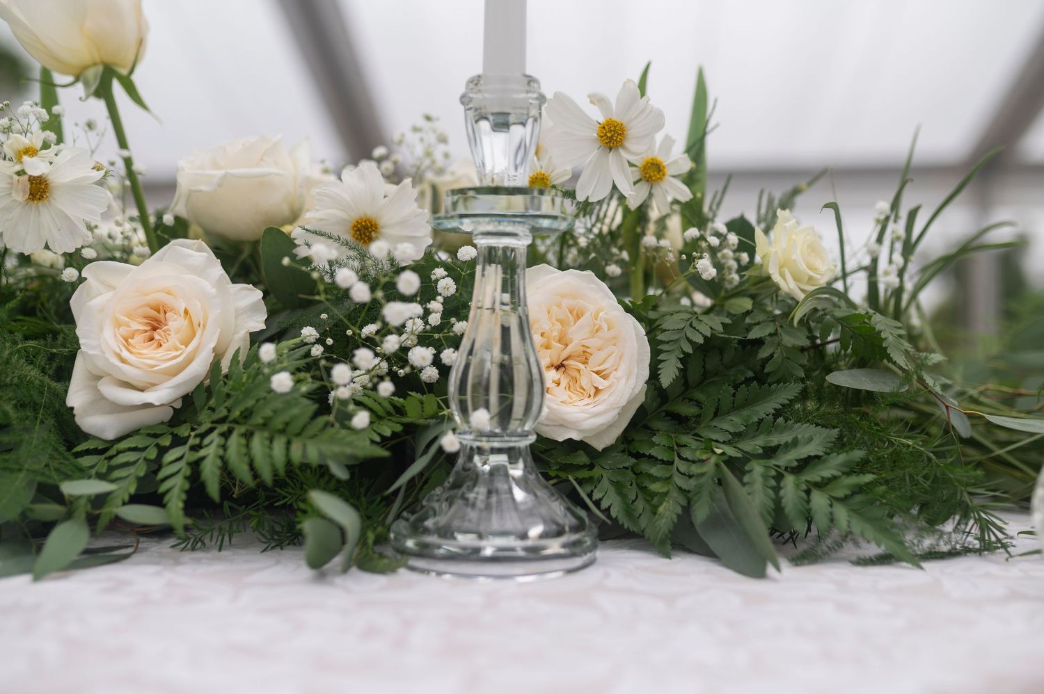 Elegant wedding tablescape with peach garden roses, baby's breath, and lush greenery surrounding crystal candleholders.