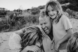 Dad and his daughters laugh hysterically at the beach during a golden hour photography session with a professional Adelaide photographer.