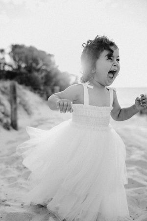 A little girl frolics and laughs at the beach at sunset in a gorgeous white tulle dress with golden sun in the background.
