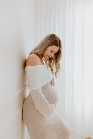 Adelaide maternity photographer, Lauren Lunn, captures mum-to-be in neutral tones smiling while holding her baby bump in a studio session.