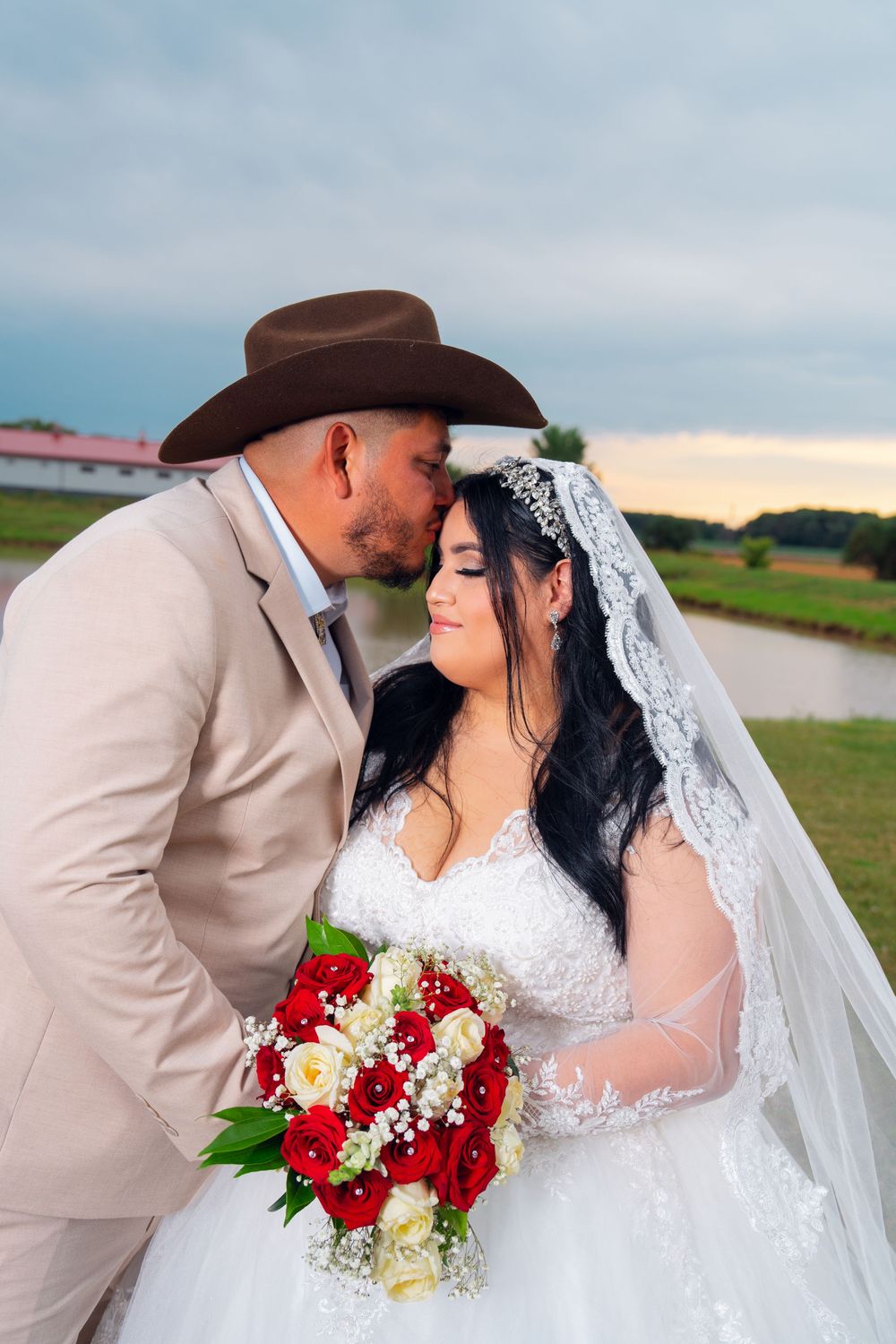 A romantic wedding couple poses with red and white roses against a sunset sky. Appleton Photographer.