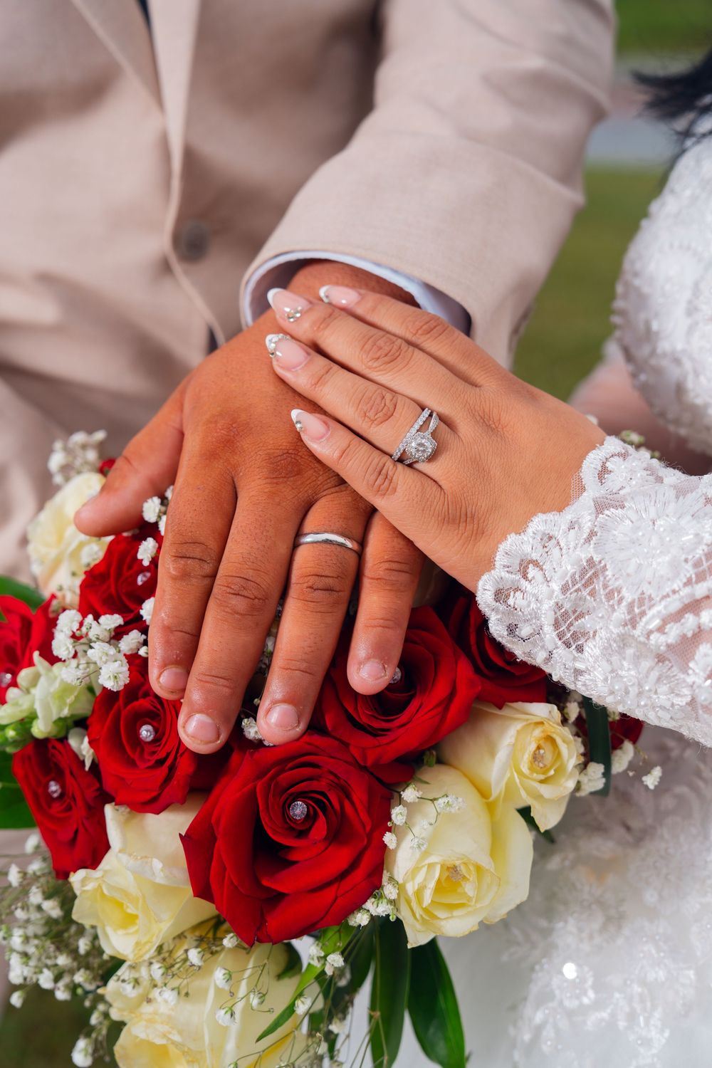 Wedding rings and hands rest on a bouquet of red and white roses with delicate lace details. Appleton Photographer.
