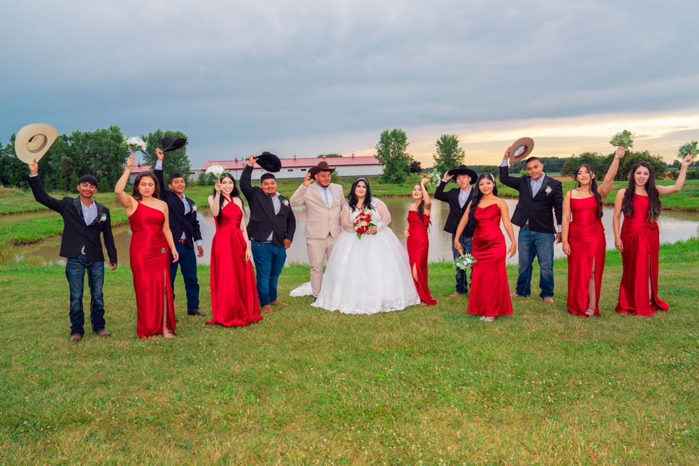 Wedding party in red dresses stands together on a grassy field during sunset. Appleton Photographer.