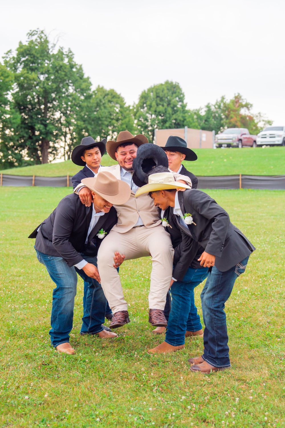 Groomsmen in cowboy hats pose playfully on grass in a fun wedding photo. Appleton Photographer.