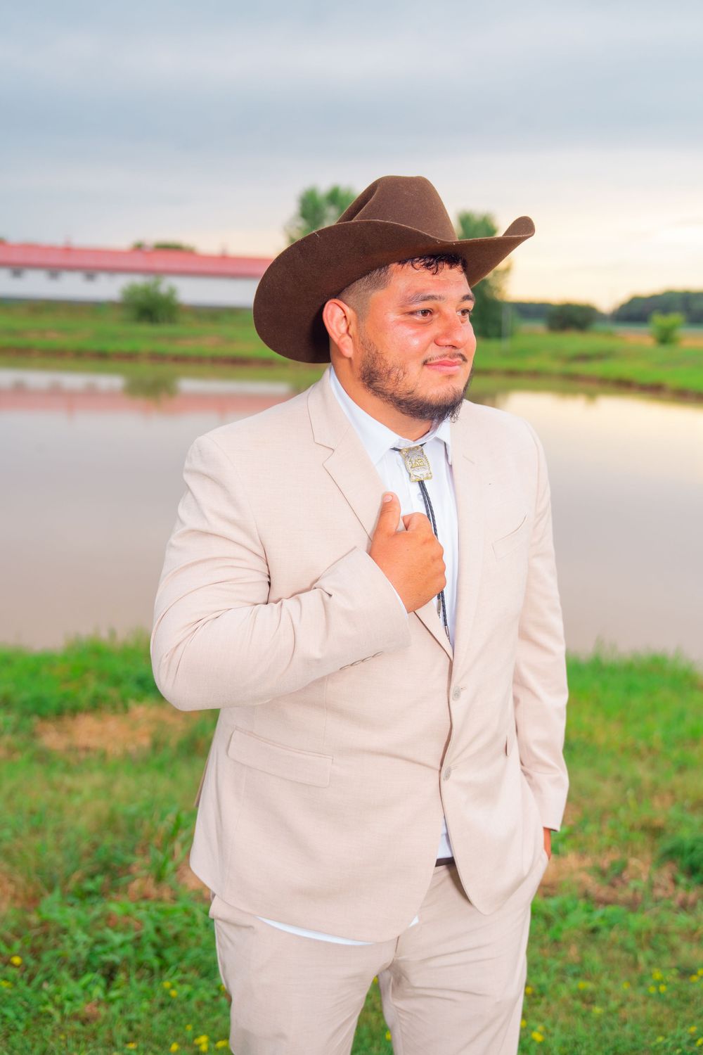Groom in beige suit and brown cowboy hat poses in outdoor setting at sunset. Appleton Photographer.