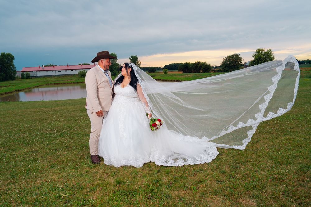 A flowing white wedding veil trails across a grassy field during sunset. Appleton Photographer.