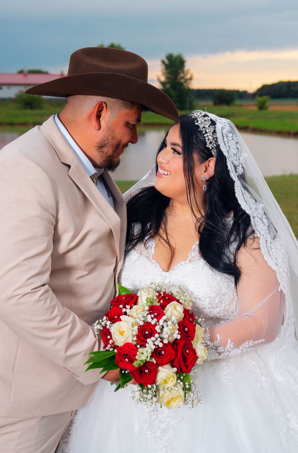 Bride and groom share romantic moment with red bouquet against lakeside backdrop. Appleton Photographer.