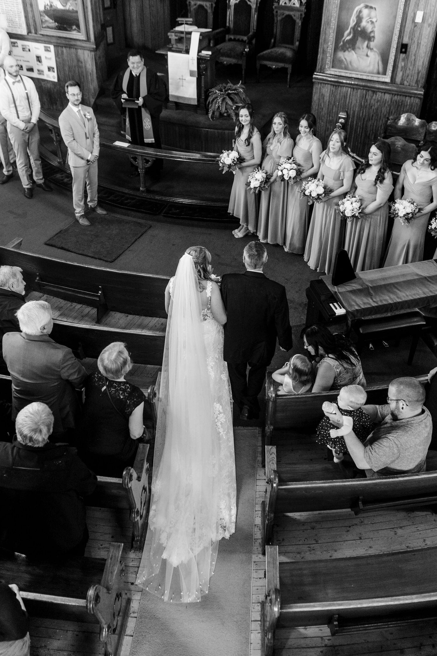 A wedding ceremony in progress at a traditional church with wedding party members and guests in black and white.