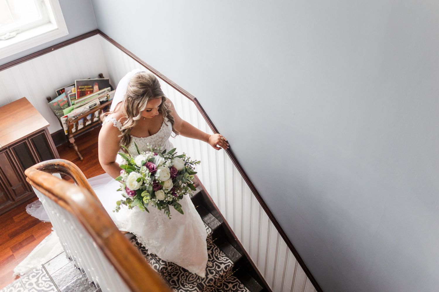 A person in a white dress holds a delicate bouquet of pink and white flowers against a wooden banister.