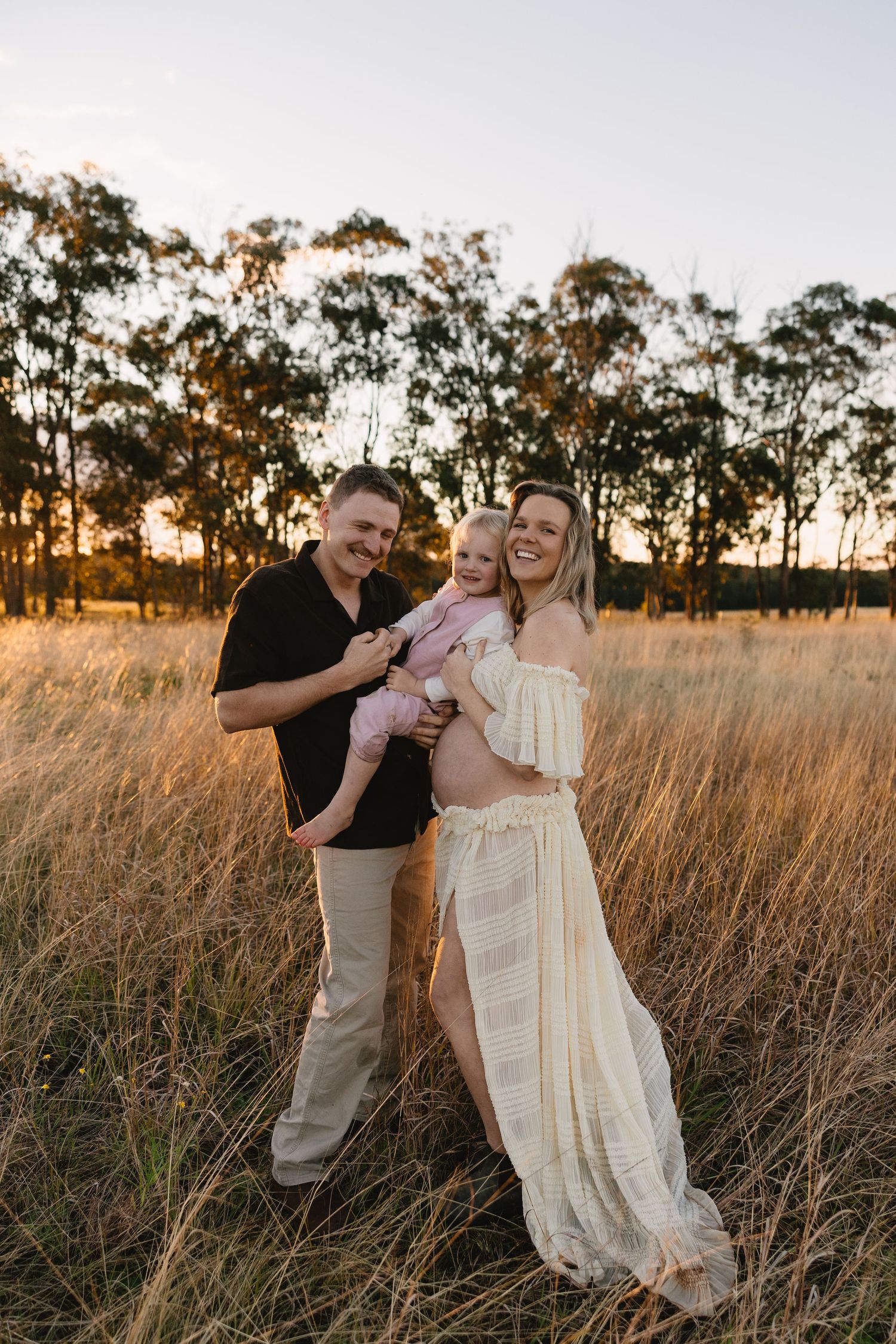 Couple sharing a joyful moment together in a sunlit field of tall golden grass during sunset.