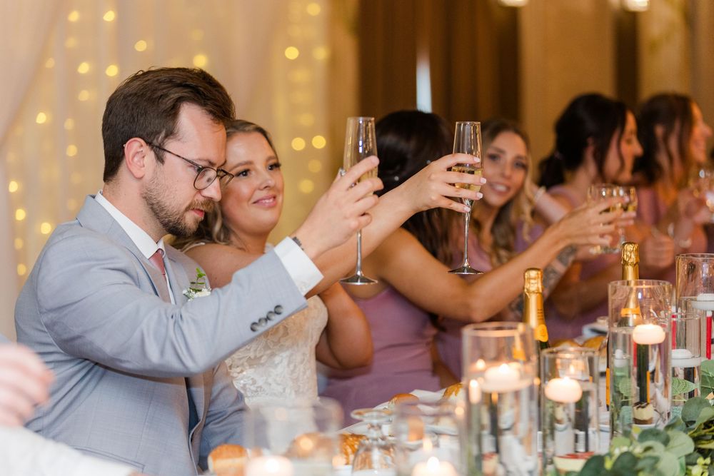 Wedding guests enjoy a celebratory dinner in a warm-lit reception hall with twinkling lights and festive atmosphere.