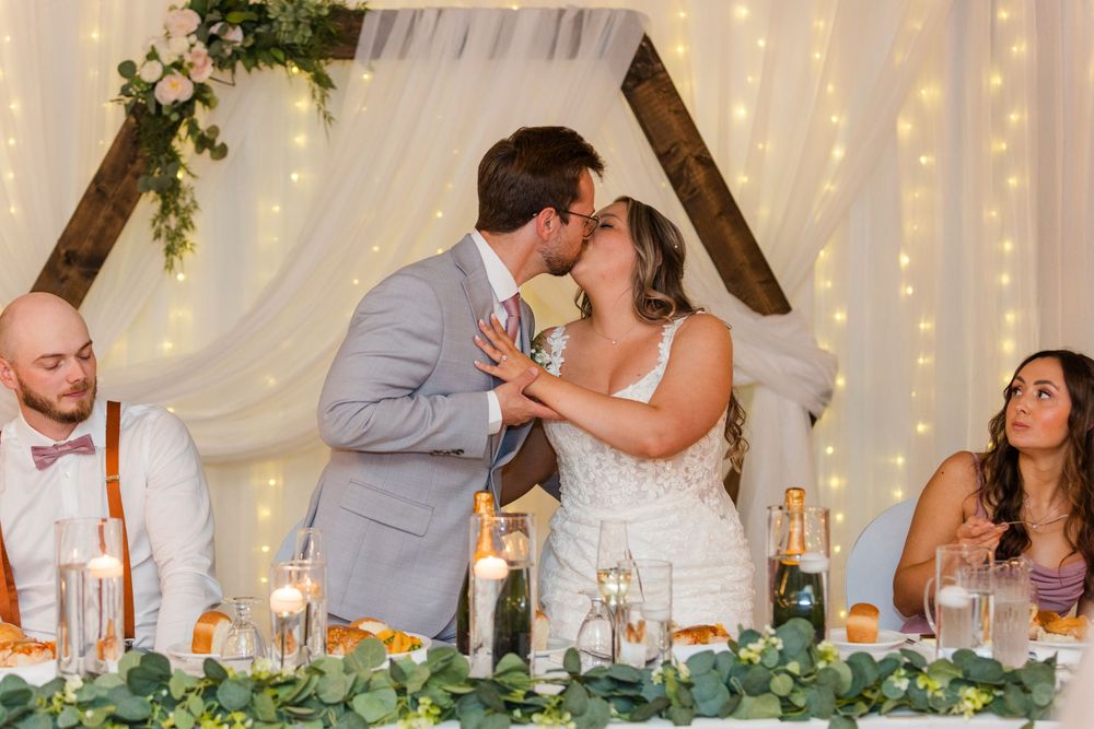 Wedding reception head table with twinkle lights and white fabric draping creating a romantic atmosphere.