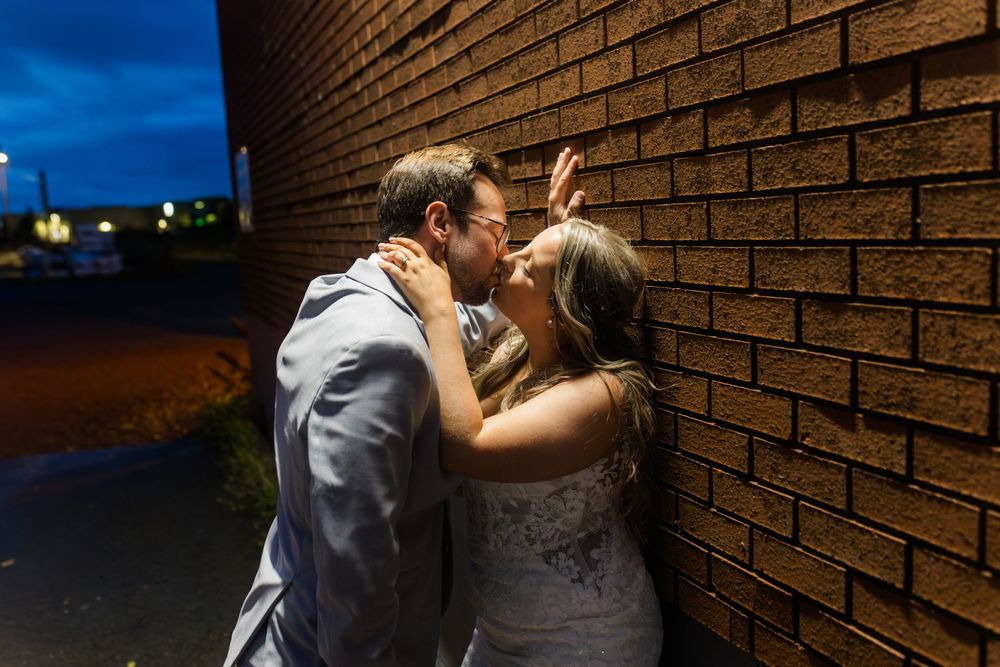 A couple shares an intimate moment against a brick wall during a romantic outdoor photo session.