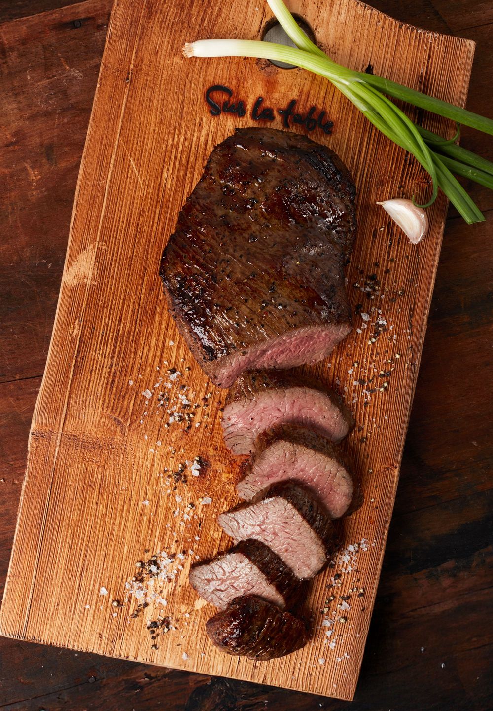 Close-up sequence of sliced medium rare steak resting on a wooden cutting board with green garnish and seasonings.