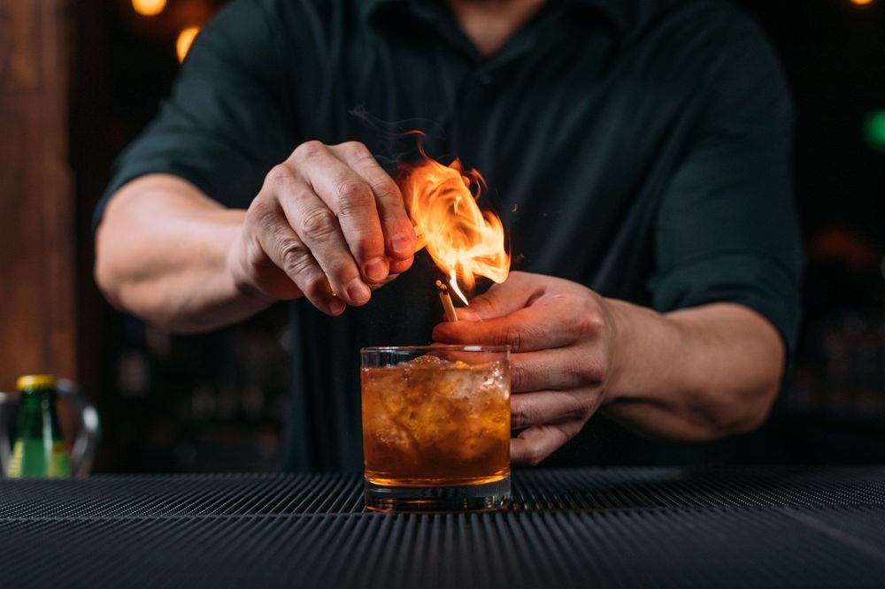 Bartender preparing craft cocktails in dark moody lighting at bar counter.
