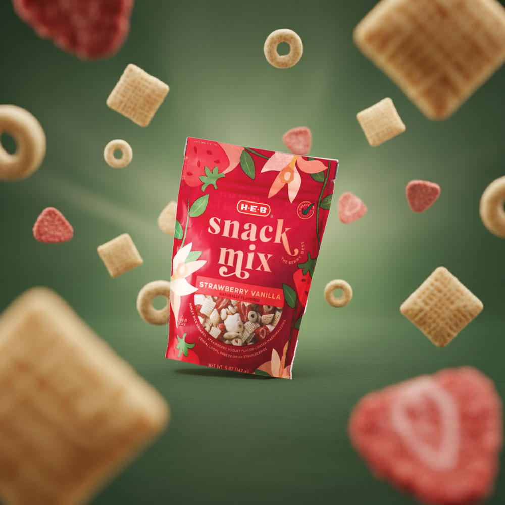 A floating red HEB snack mix package surrounded by heart-shaped candies and cereal pieces on a green gradient background.