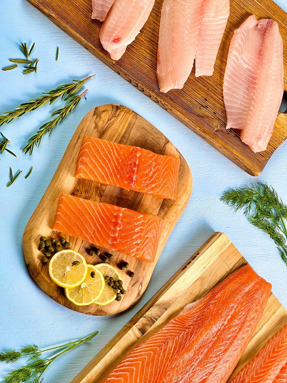 Fresh salmon fillets arranged on wooden serving boards with herbs and lemon garnish.