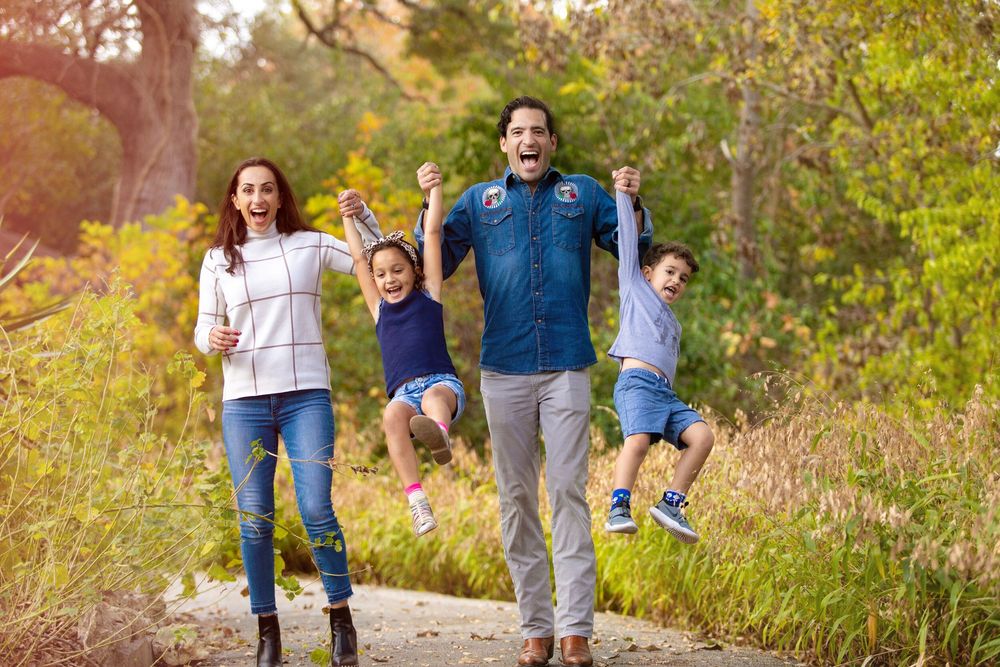 A playful outdoor photoshoot in a sunny natural setting with tall grass and trees.