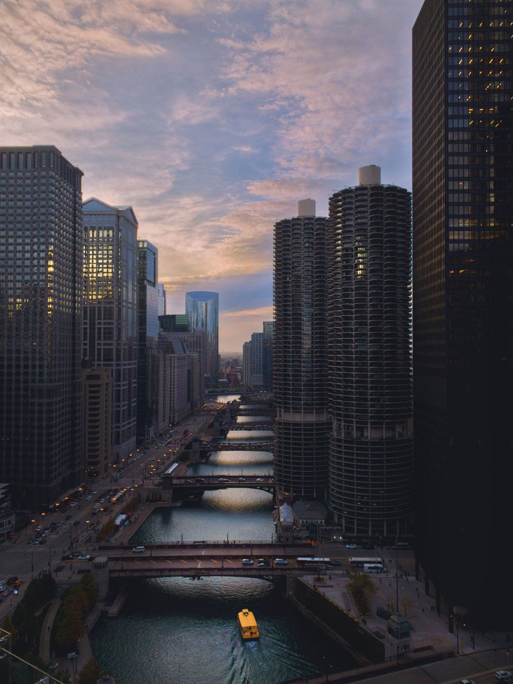 Chicago River winding through downtown skyscrapers at sunset with multiple bridges crossing.