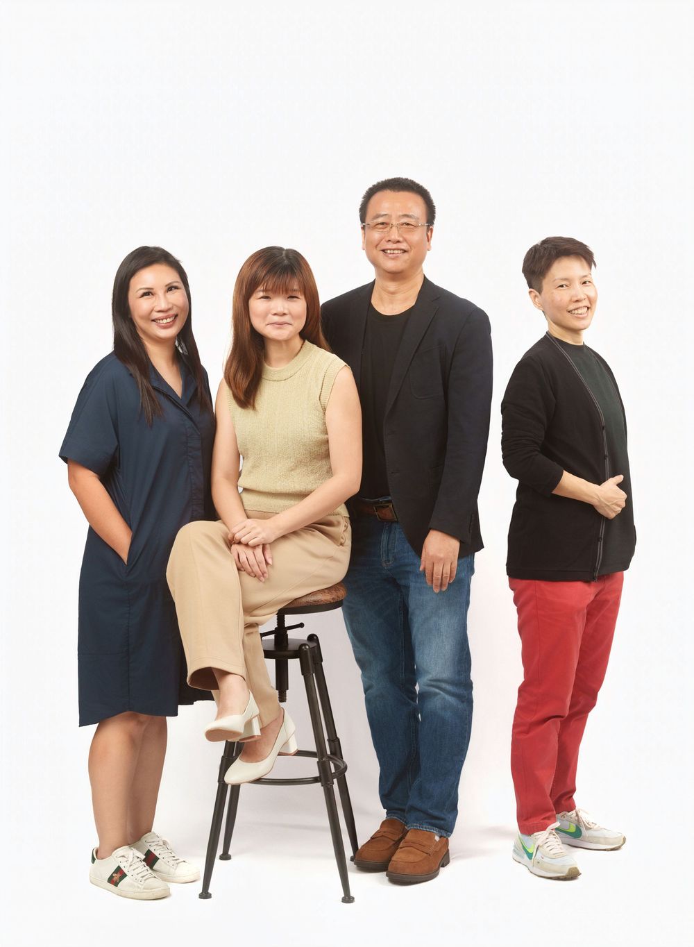 A group of people arranged in a row against a white background with black and beige casual attire.
