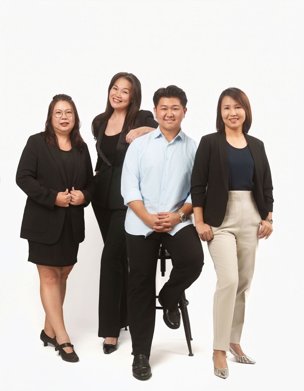 A group in professional business attire poses playfully while sitting on white stools against a plain background.