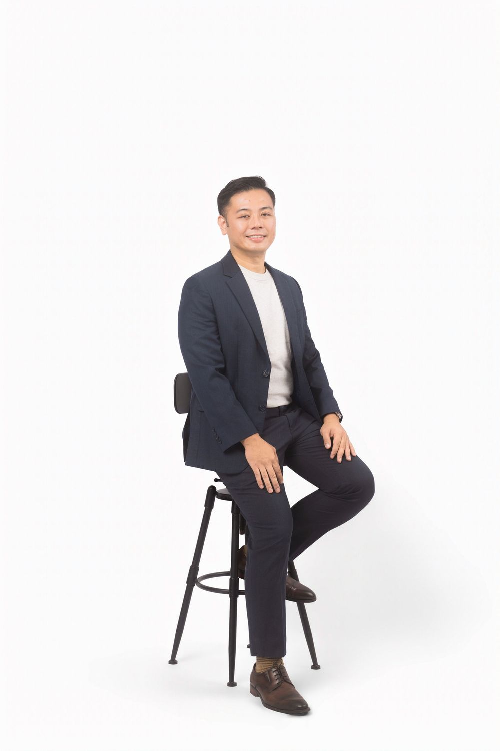 Professional seated on a black chair wearing a dark suit and white shirt against white background.